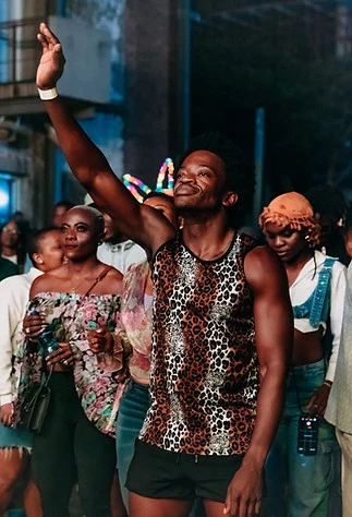 A man in a leopard print vest raising an arm in the crowd